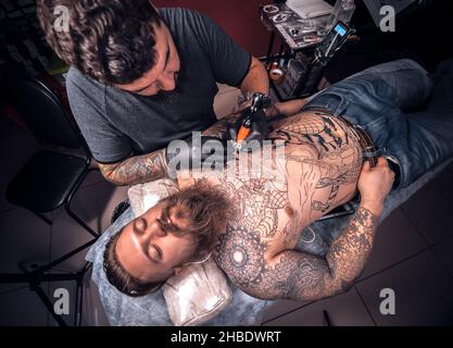 Tatuista che lavora su pistola professionale tatuaggio in salone tatoo Foto Stock