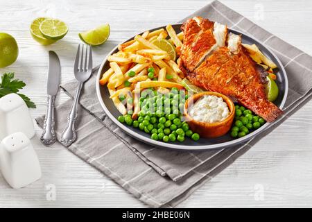 Scorfano fritto su un piatto con patatine fritte, piselli verdi bolliti, salsa tartara e fettine di lime, vista orizzontale dall'alto Foto Stock