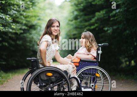 Ritratto di giovani Signore caucasiche in carrozzine seduti di fronte l'uno all'altro nel parco estivo e guardando la macchina fotografica. Concetto di persone con disabilità e stili di vita. Foto Stock