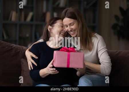 Figlia adulta affettuosa abbraccia eccitata madre più anziana dare regalo di compleanno Foto Stock