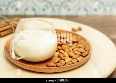 Latte non diario. Composizione di cibo vegano con una tazza di latte di mandorle e noci di mandorle su un piatto di legno e bastoncini di cannella su una cucina ecologica. Rustico Foto Stock