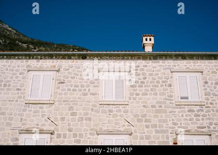 Facciata dell'edificio in pietra grigia con persiane bianche sulle finestre Foto Stock