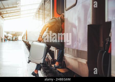Bell'uomo nero calvo bearded a bordo di un treno. Uomo d'affari africano sulla stazione ferroviaria con una valigia grigia e in abiti sociali: Pelle s Foto Stock