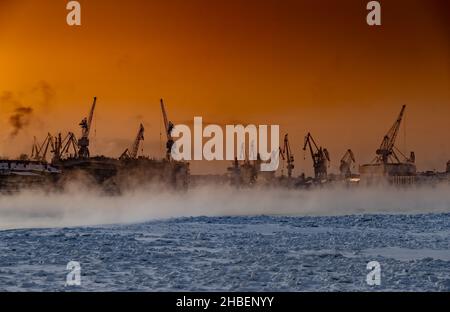 La costruzione di rompighiaccio nucleare al tramonto magico, gru del cantiere Baltico in una gelida giornata invernale, vapore sul fiume Neva, liscio Foto Stock