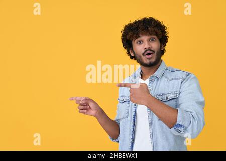 Stupito sorpreso giovane indiano che punta su sfondo giallo. Foto Stock