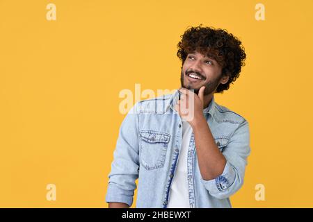 Curioso giovane indiano che guarda, pensa, pianifica su sfondo giallo. Foto Stock