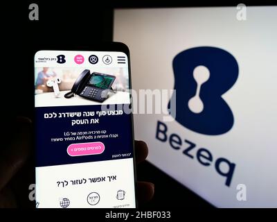 Persona che detiene il cellulare con il sito web di Bezeq The Israeli Telecommunication Corp Ltd. Su schermo con il logo. Concentrarsi sul centro del display del telefono. Foto Stock