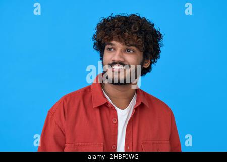 Felice sorridente giovane indiano che guarda, sognando su sfondo blu. Foto Stock