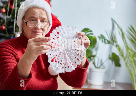 donna anziana tiene un fiocco di neve tagliato di carta nelle sue mani. Decorazione per il nuovo anno e Natale. Foto Stock
