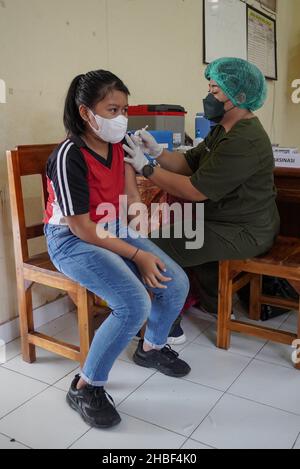 Denpasar, Indonesia. 15th Dic 2021. Un operatore sanitario somministra una dose del vaccino Sinovac covid-19 ad uno studente. La Scuola elementare 33 di Dangin Puri, Denpasar, Bali, ha iniziato la vaccinazione di Covid-19 per gli studenti di 6-11 anni, in quanto l'Indonesia continua ad aumentare il numero di vaccinazioni dei cittadini al fine di impedire che il coronavirus Covid-19 si diffonda ulteriormente. Credit: SOPA Images Limited/Alamy Live News Foto Stock