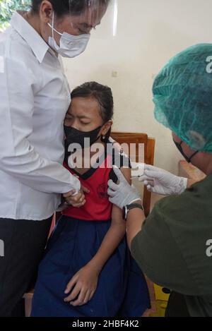 Denpasar, Indonesia. 15th Dic 2021. Un operatore sanitario somministra una dose del vaccino Sinovac covid-19 ad uno studente. La Scuola elementare 33 di Dangin Puri, Denpasar, Bali, ha iniziato la vaccinazione di Covid-19 per gli studenti di 6-11 anni, in quanto l'Indonesia continua ad aumentare il numero di vaccinazioni dei cittadini al fine di impedire che il coronavirus Covid-19 si diffonda ulteriormente. Credit: SOPA Images Limited/Alamy Live News Foto Stock