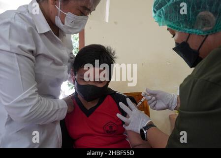 Denpasar, Bali, Indonesia. 15th Dic 2021. Un operatore sanitario somministra una dose del vaccino Sinovac covid-19 ad uno studente. La Scuola elementare 33 di Dangin Puri, Denpasar, Bali, ha iniziato la vaccinazione di Covid-19 per gli studenti di 6-11 anni, in quanto l'Indonesia continua ad aumentare il numero di vaccinazioni dei cittadini al fine di impedire che il coronavirus Covid-19 si diffonda ulteriormente. (Credit Image: © Dicky Bisinglasi/SOPA Images via ZUMA Press Wire) Foto Stock