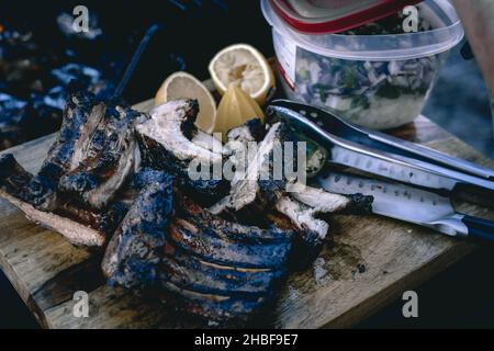 Un bicchierino di costolette grigliate e affettate sul vassoio di legno con limoni e insalata di cipolle Foto Stock