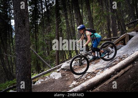 Banff Alberta Canada, 04 2021 luglio: Una ragazza mountain bike scende ripido terreno roccioso su un sentiero designato. Foto Stock