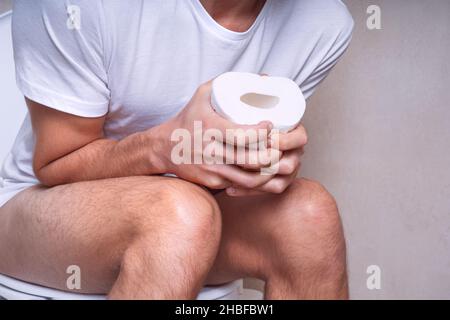 Uomo seduto sul gabinetto e che soffre di costipazione, diarrea, mal di stomaco o crampi Foto Stock