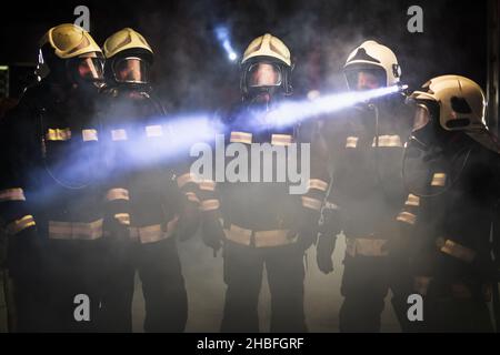 Gruppo di vigili del fuoco professionisti. Vigili del fuoco che indossano uniformi, caschi protettivi e maschere per ossigeno. Fumo sullo sfondo. Foto Stock