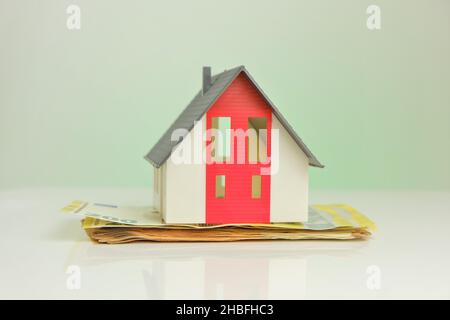 Acquisto e costruzione di una casa. Casa e soldi. Casa mock con tetto grigio su sfondo banconote in euro. Foto Stock