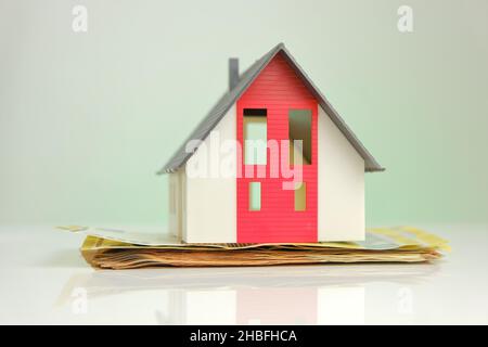 Acquisto e costruzione di una casa. Casa e soldi. Casa mock con tetto su sfondo banconote in euro. Foto Stock
