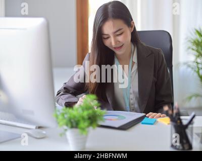Attraente contabile femminile asiatica o banchiere che analizza le informazioni di dati finanziari su un lavoro di ufficio. Donna d'affari lavora in ufficio Foto Stock