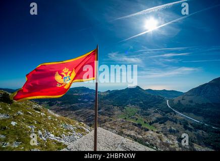 Sulla cima del monte Lovcen, la maestosa bandiera nazionale rossa dello stato balcanico che sbatte nel vento, contro cieli limpidi e soleggiati blu di fine estate Foto Stock