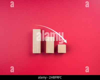 Trend grafico verso il basso. Concetto di crisi aziendale. Freccia giù su tre blocchi di legno grafico passi su sfondo rosso con spazio di copia, stile minimal. Foto Stock