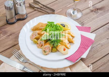 Crepes farcito con pesce, formaggio e caviale rosso, guarnito con erbe su un piatto bianco su sfondo di legno scuro Foto Stock