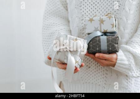 Una ragazza in maglione bianco contiene regali di festa. Le mani femminili stanno tenendo le scatole di festa. Il concetto di preparazione delle vacanze Foto Stock
