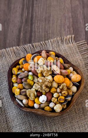 Noci miste, croccanti, secche in un piatto di legno su tavola di legno, con tovagliolo di iuta Foto Stock