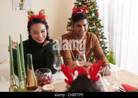 Felice giovane coppia variegata in corna di renne godendo cena di Natale con la famiglia Foto Stock