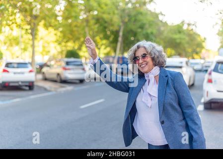 donna d'affari matura che chiama un taxi per strada Foto Stock