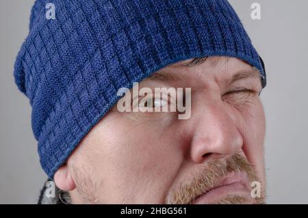 Guardami negli occhi. Primo piano sull'occhio marrone di un uomo. Un uomo cresciuto in un cappello blu grimaces. Foto Stock