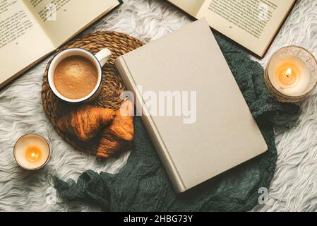 Vista dall'alto di libri, tazza di caffè, croissant e candele su uno sfondo bianco pelliccia coperta. Messa a fuoco selettiva Foto Stock