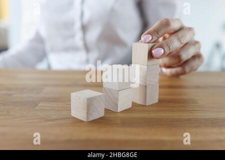 Femmina che mette mattoni di legno sulla parte superiore della pila, torre di costruzione Foto Stock