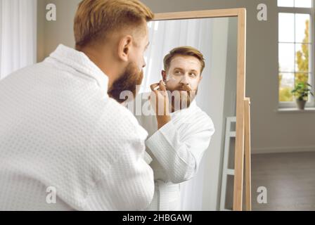Uomo adulto che si prende cura di se stesso e applica la maschera al suo viso con pennello cosmetico. Foto Stock
