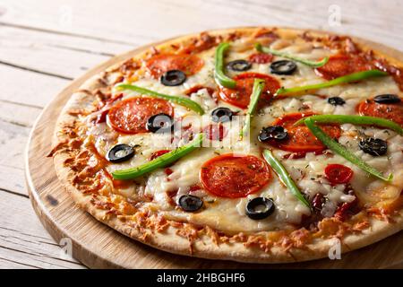 Pizza tradizionale suprema su un rustico tavolo di legno Foto Stock