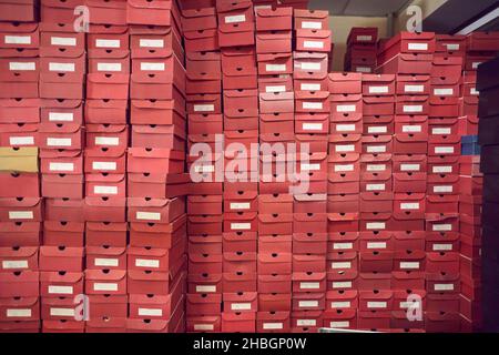 Grande parete di scatole in cartone rosso con calzature impilate in un magazzino di fabbrica Foto Stock