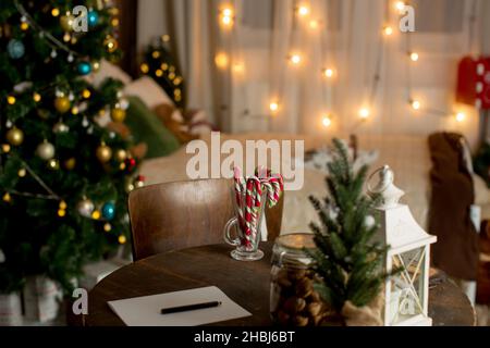 Vecchio tavolo in legno con decorazione e sedia di natale, carta preparata per la scrittura, caramelle e noci sul tavolo e decorazione in camera Foto Stock