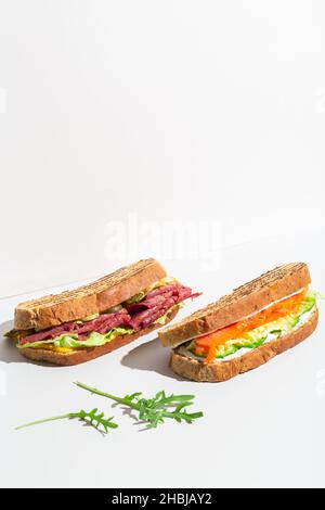 Due sandwich con salmone, prosciutto, formaggio e insalata all'ombra grigia scura Foto Stock