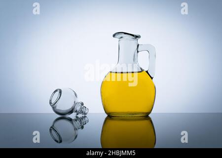 Bottiglia d'olio d'oliva, aroma di insalata vegetale. Sfondo grigio. Olio di cottura giallo in un vaso di vetro Foto Stock