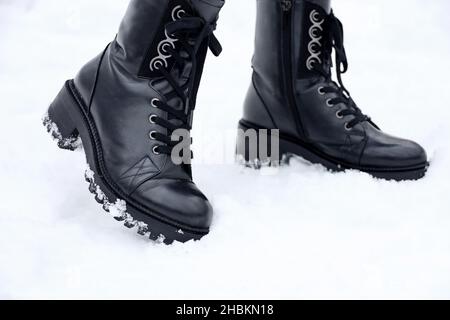 Gambe femminili in pelle nera stivali con lacci sulla neve. Donna sulla strada invernale, scarpe calde per il freddo Foto Stock