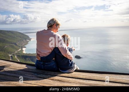 Madre e figlio di 3 anni si abbraccia e si gode la splendida vista sull'oceano, Portogallo Foto Stock