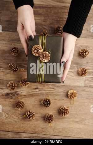 Mani di donna che danno avvolti regalo di Capodanno decorato con coni di pino Foto Stock