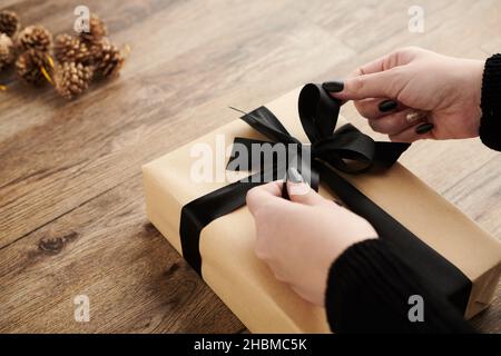 Mani di donna che legano arco nero su regalo di Natale avvolto per il suo amato uno Foto Stock