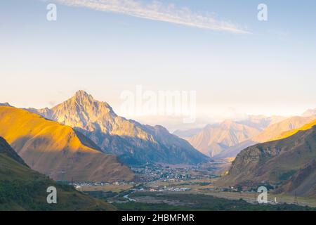 Vista panoramica sui piccoli villaggi arrotondati da montagne lungo la strada principale nel parco nazionale di Kazbegi Foto Stock