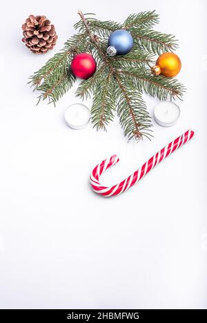 Natale e nuovo anno piatto laici: Ramo di abete verde, cono, rosso, blu e giallo palle, due candele e caramello caramella su sfondo bianco isolato. Foto Stock