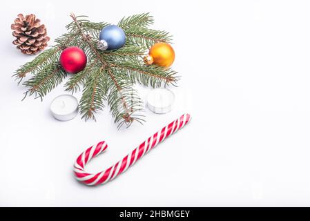 Natale e nuovo anno piatto laici: Ramo di abete verde, cono, rosso, blu e giallo palle, due candele e caramello caramella su sfondo bianco isolato. Foto Stock