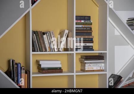 Russia, Mosca, dicembre 20211. Mensole bianche di forma insolita con libri. Interni domestici. Foto Stock