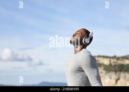 Uomo rilassato con pelle nera indossando cuffie senza fili meditando ascolto audioguida Foto Stock