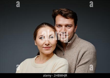 Ritratto di coppia adulta che abbraccia e guarda la fotocamera in studio contro il backckground nero Foto Stock