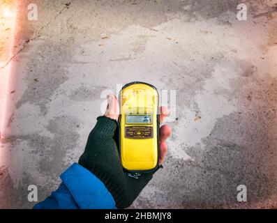 Immagine di sfondo di cemento e radiazione intorno al contatore dosimetro/geiger nelle mani delle persone con schermo vuoto. Concezione dell'emergenza radioattiva. Foto Stock